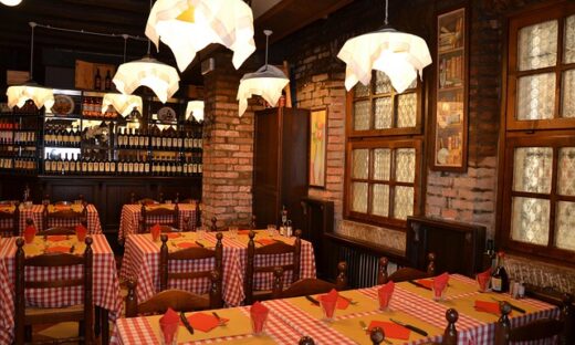 Cozy brick-walled restaurant dining area with red-and-white checkered tables, wooden chairs, and warm pendant lighting.