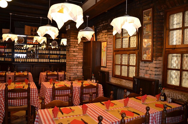 Cozy brick-walled restaurant dining area with red-and-white checkered tables, wooden chairs, and warm pendant lighting.