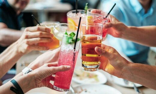 Group of people toasting with colorful cocktails at a dining table, raising glasses together.