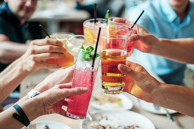 Group of people toasting with colorful cocktails at a dining table, raising glasses together.