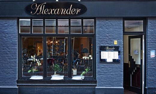 Restaurant storefront named Alexander with a large front window and a menu board beside the door.