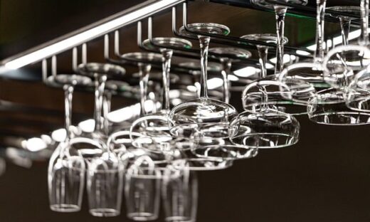 Rows of wine glasses hanging upside down from a rack above a bar area, reflecting light.