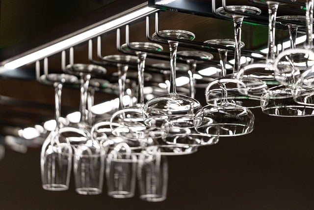 Rows of wine glasses hanging upside down from a rack above a bar area, reflecting light.