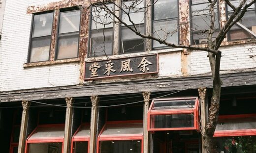 Old storefront with peeling paint, rusted sign, and red-framed windows, on a tree-lined street.
