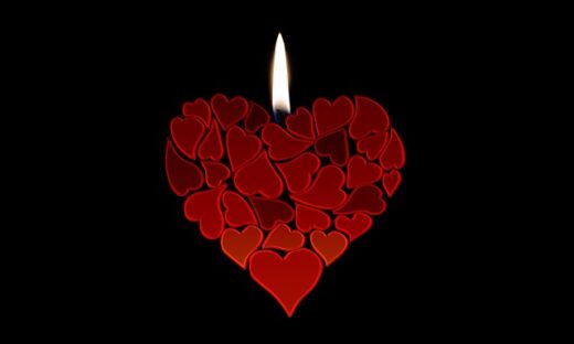 Heart made from many small red hearts with a lit candle flame above, set against a black background.