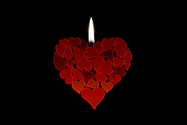Heart made from many small red hearts with a lit candle flame above, set against a black background.